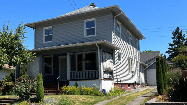 Gray two-story house with a porch and garden, representing homes in Portland for cash sale opportunities.