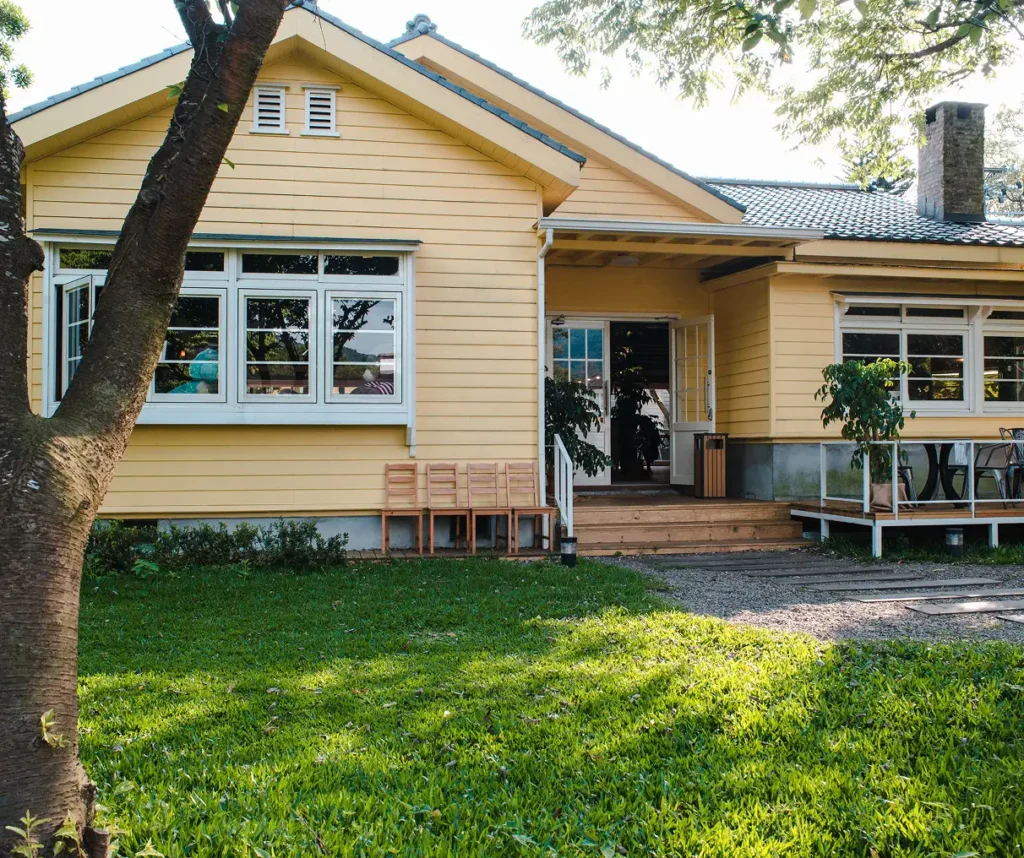 Yellow house with a welcoming porch and large windows, surrounded by green grass, illustrating a potential home for quick cash sale in Portland.
